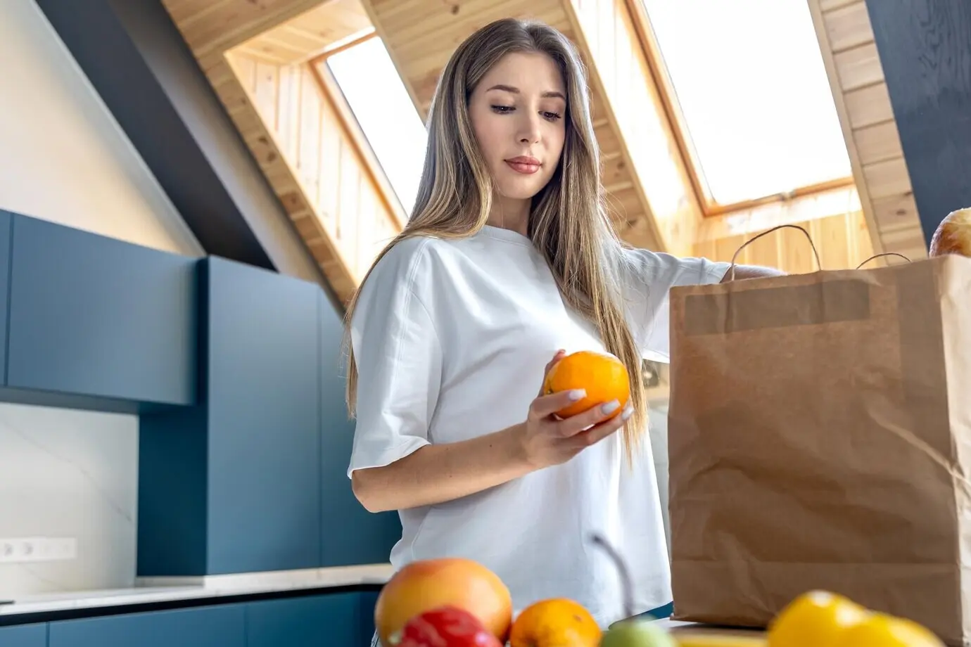 A woman holding an orange in a bright kitchen interior with natural products.
